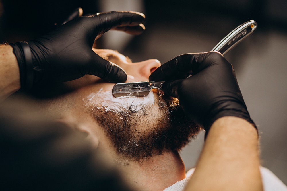 Handsome man cutting beard at a barber shop salon