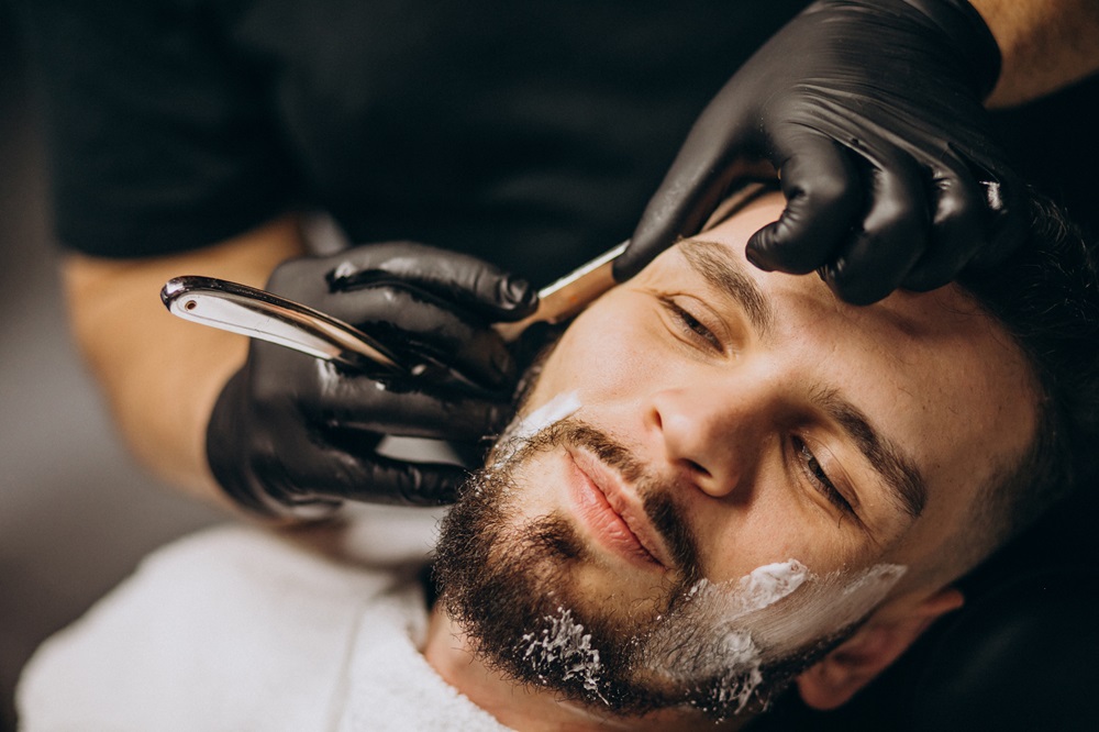 Handsome man cutting beard at a barber shop salon